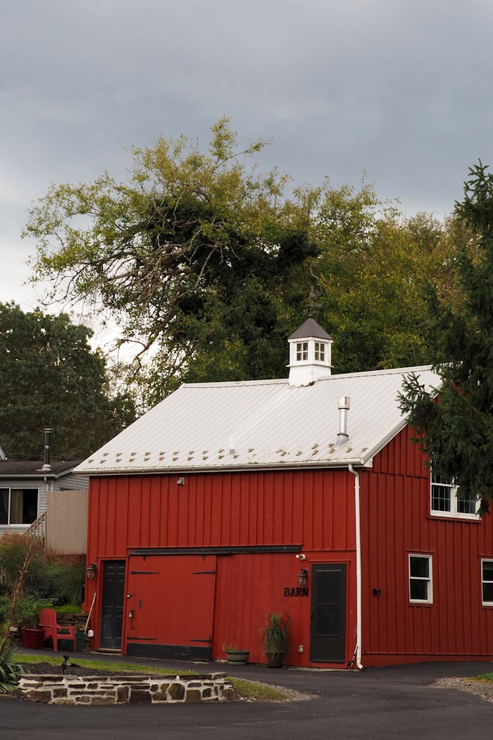 Red barn with white roof nestled among trees in Doylestown, PA under a cloudy sky.